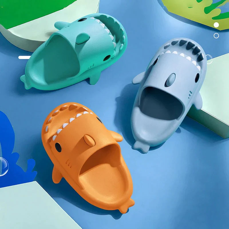 Three shark-shaped children's shoes in orange, green, and blue on a blue background.